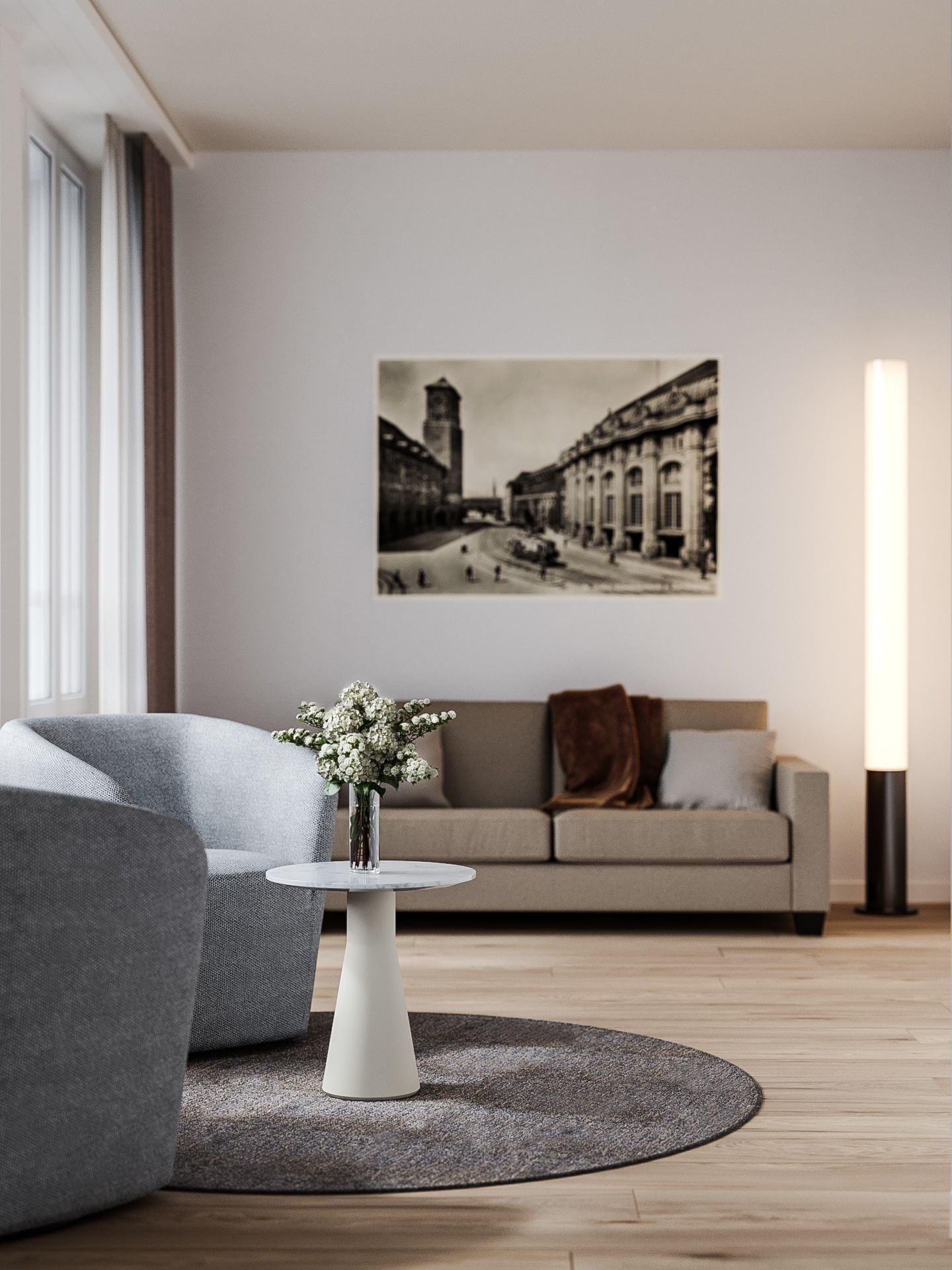 A modern living room with a grey sofa, a round coffee table with a vase of flowers, and a large framed photograph on the wall.