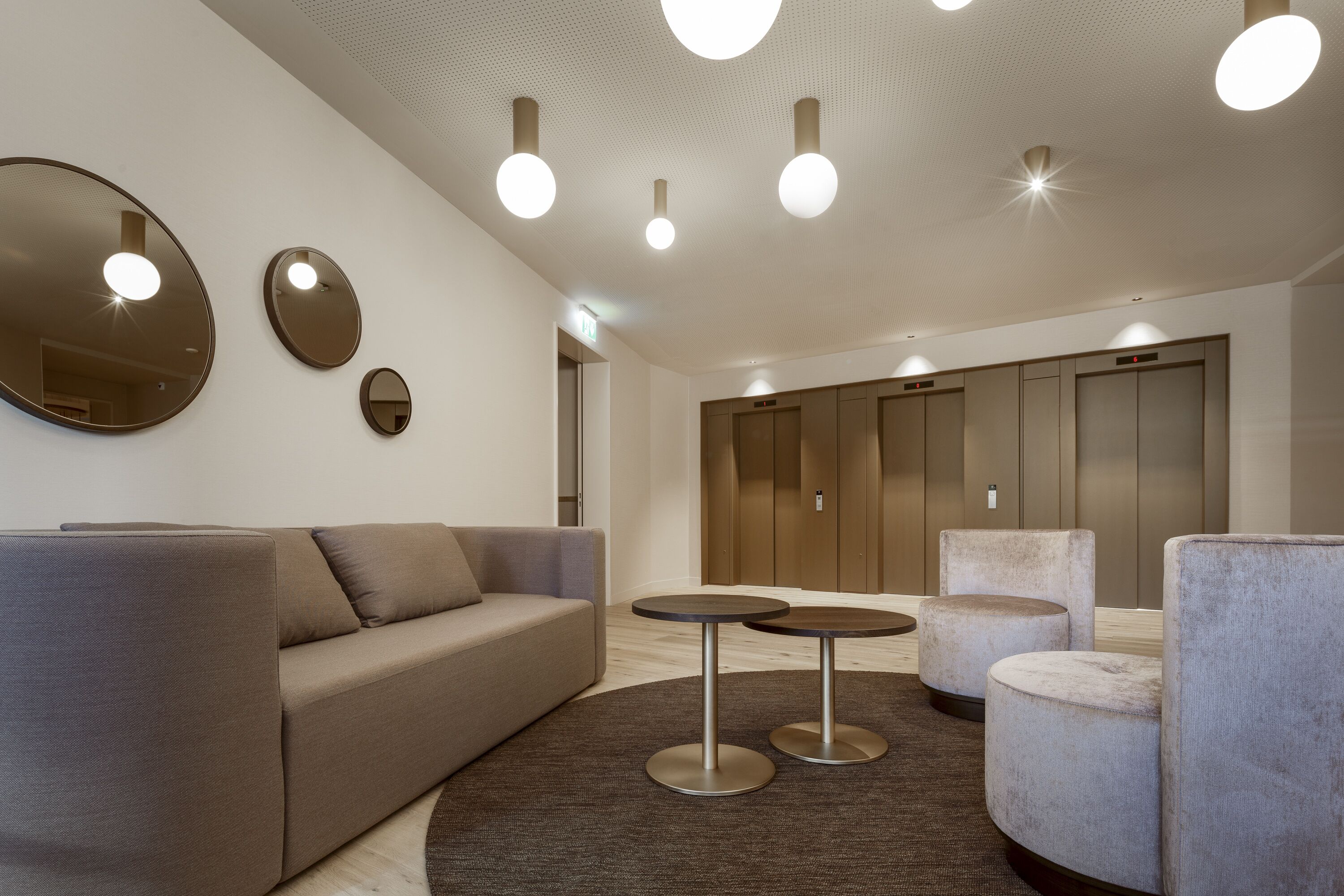 A modern lobby with a sofa, round tables, and a large mirror.
