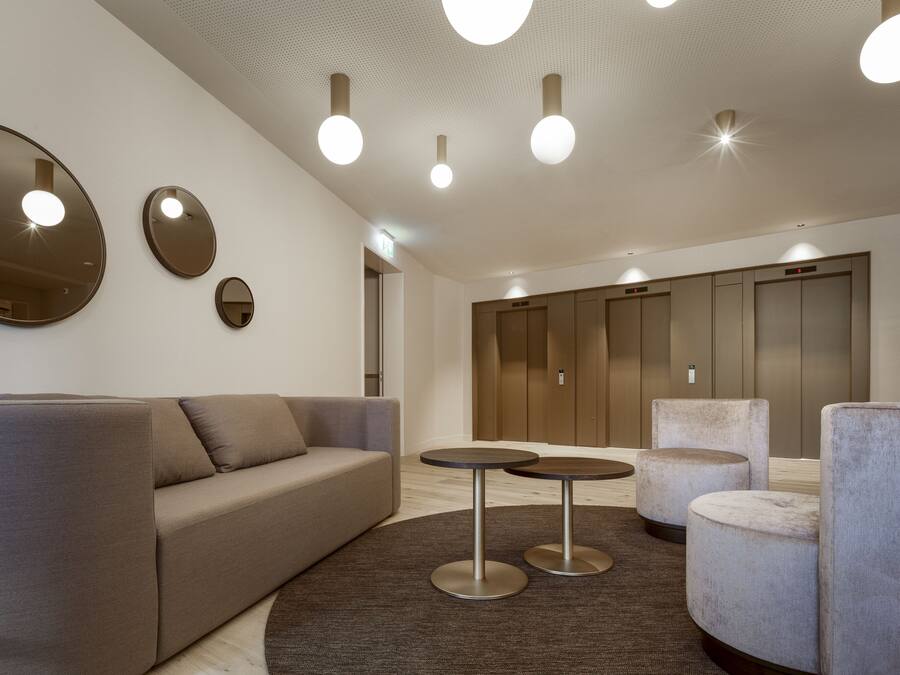 A modern lobby with a sofa, round tables, and a large mirror.