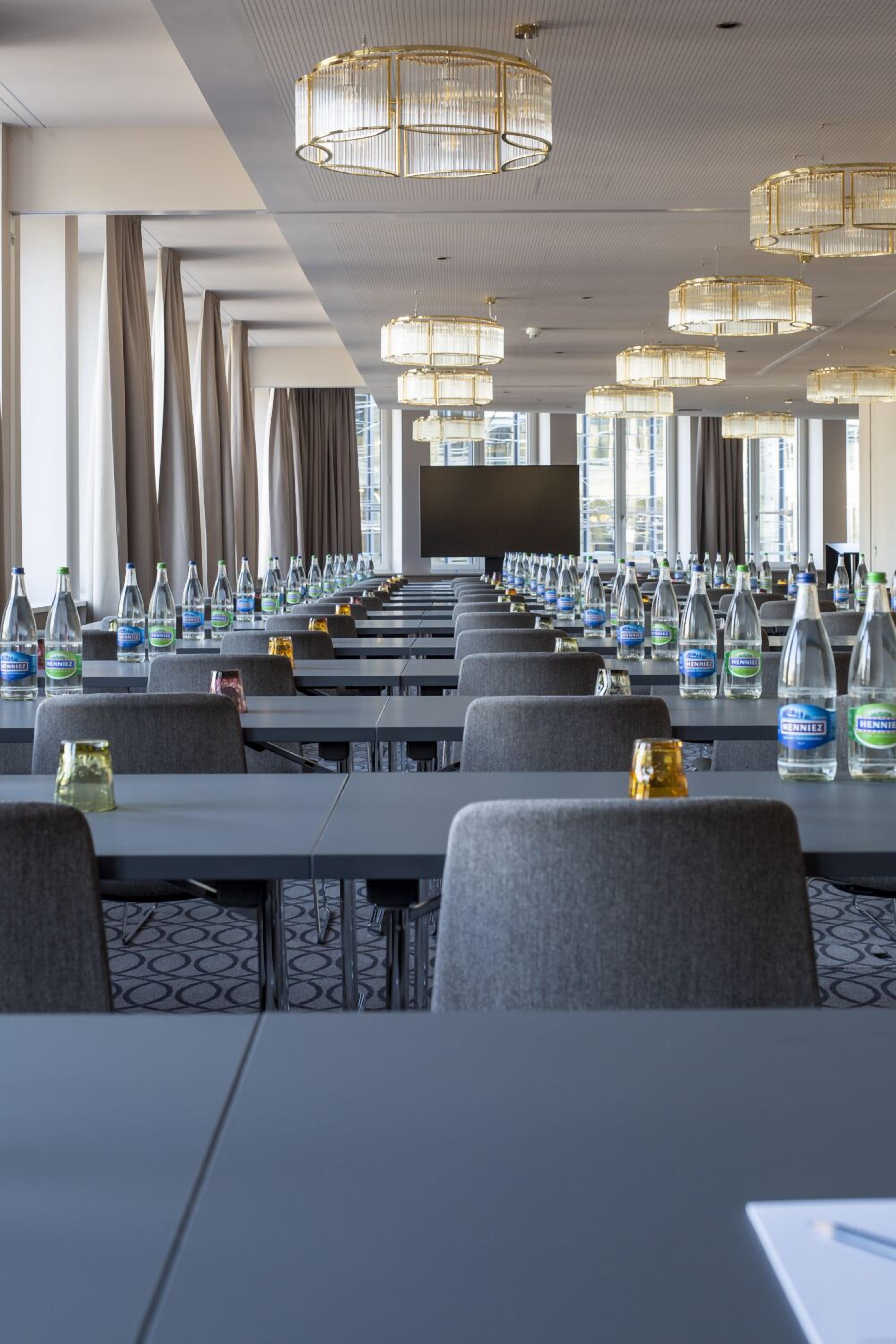 A conference room with rows of tables, chairs, and bottled water.