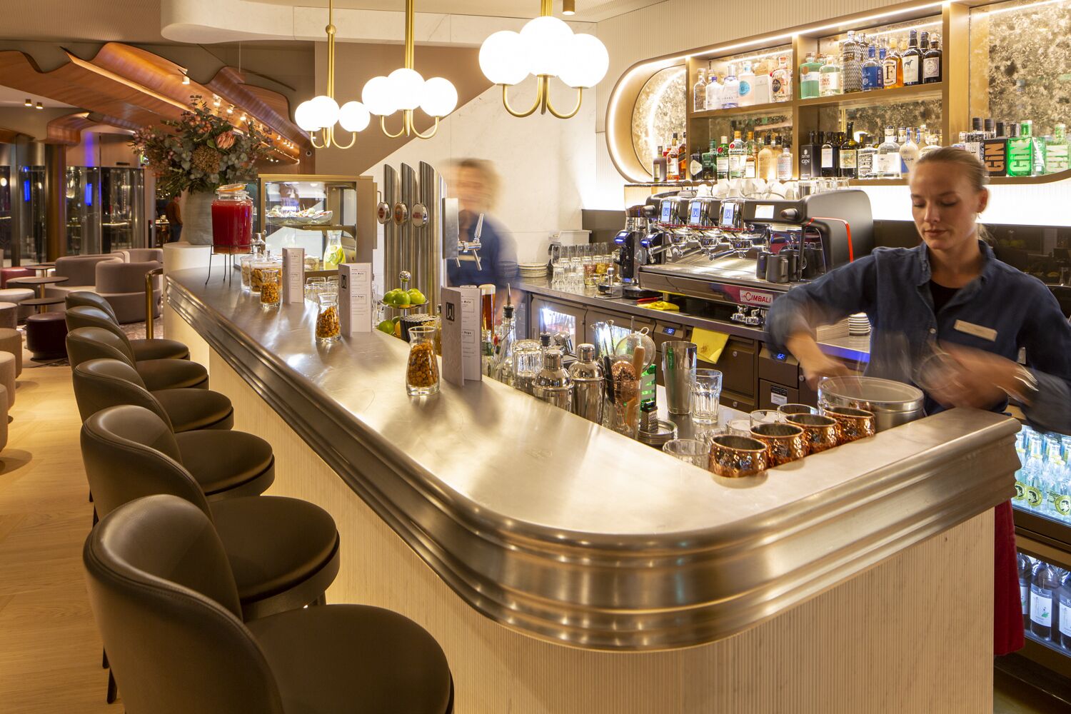 A bar area with a curved counter, bar stools, and a variety of bottles and glasses.