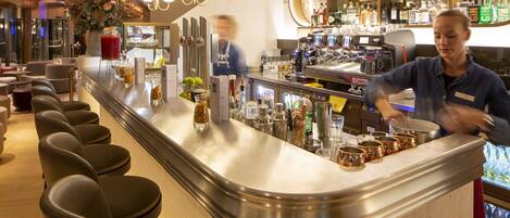 A bar area with a curved counter, bar stools, and a variety of bottles and glasses.