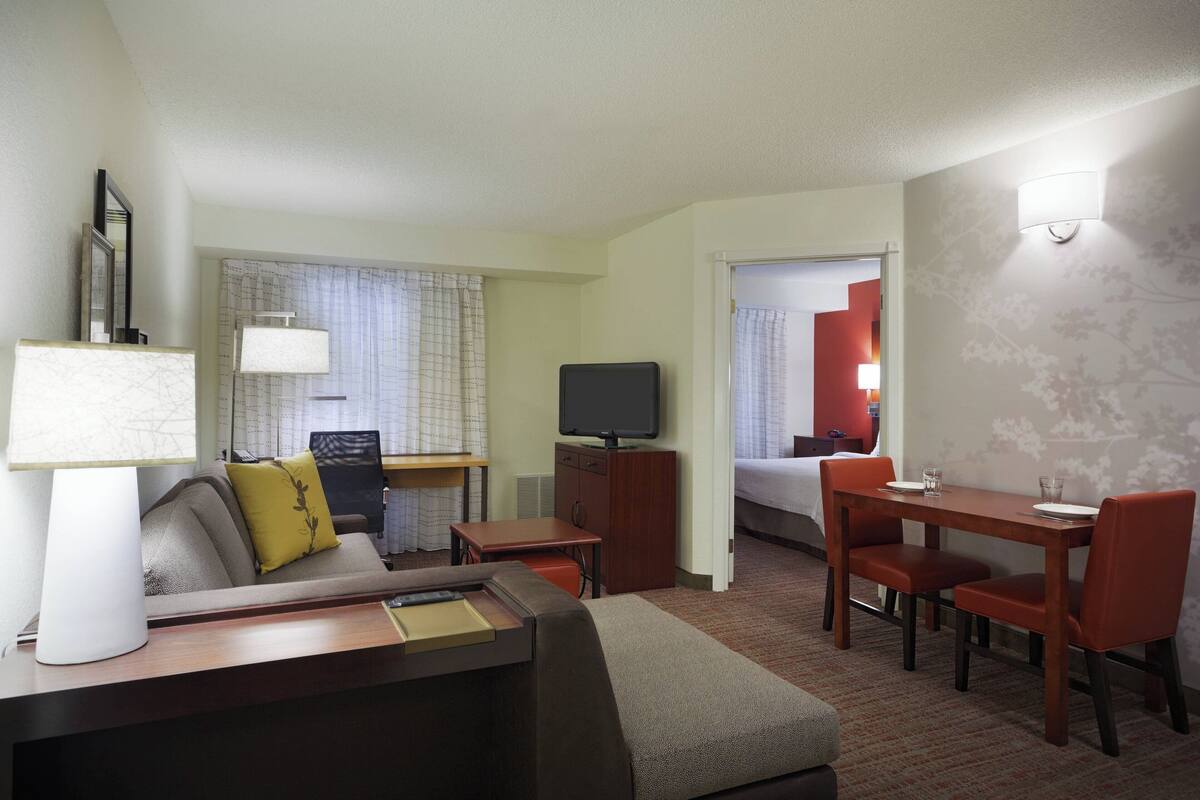A hotel room with a bed, a desk with a chair, a television, and a dining area with chairs and a table.