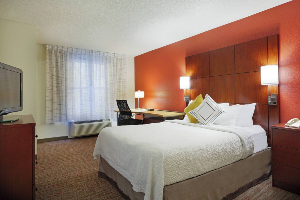 A hotel room with a bed, a desk, a chair, a television, and a window with curtains.