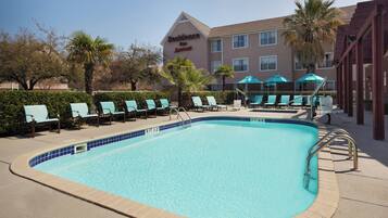 Una piscina al aire libre, sombrillas, sillones reclinables de piscina