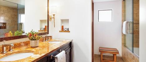 Une salle de bain avec deux lavabos, un grand miroir, une douche et un petit banc en bois.