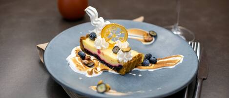 A dessert on a plate with whipped cream, blueberries, and a slice of cake, accompanied by a glass of red wine.