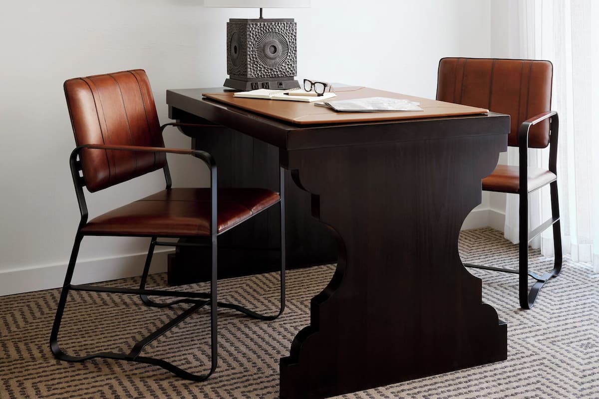 A dining area with a dark wooden table, two leather chairs, a white table lamp, and framed pictures on the wall.