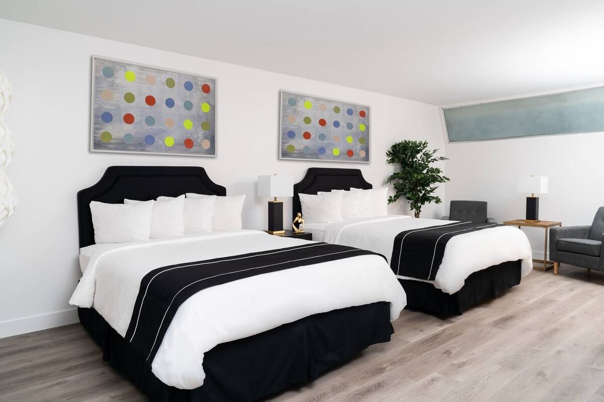 A hotel room with two beds, a desk, a chair, and artwork on the walls.
