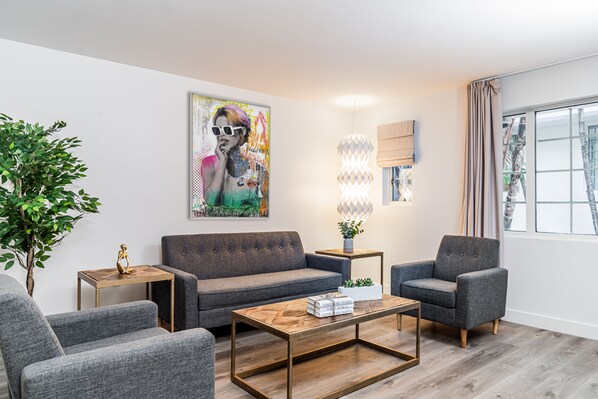 Una sala moderna con un sofá gris, dos sillones, una mesa de centro de madera y una planta en maceta.
