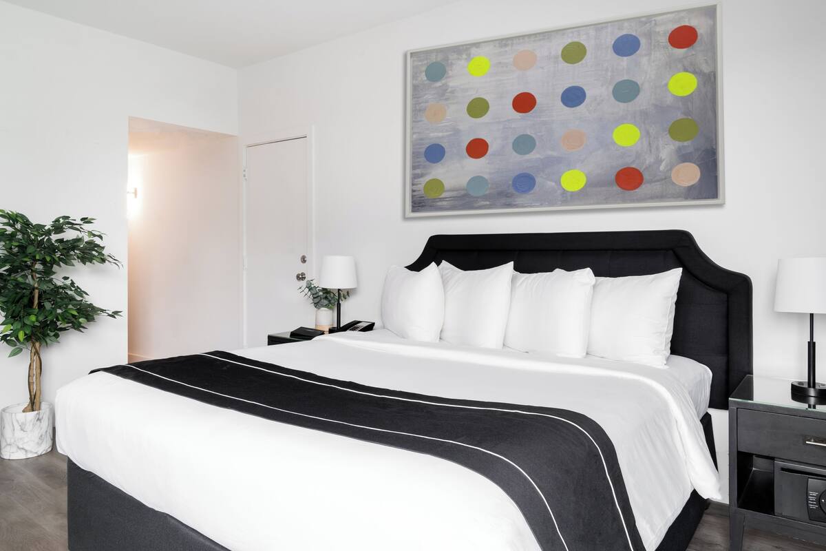 A modern hotel room with a large bed, a nightstand, a lamp, and a potted plant.