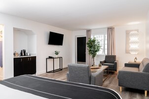 Una habitación de hotel moderna con cama, escritorio, silla, sofá y televisión montada en la pared.
