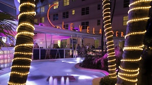 Un hotel con piscina, palmeras adornadas con luces y un letrero de neón.