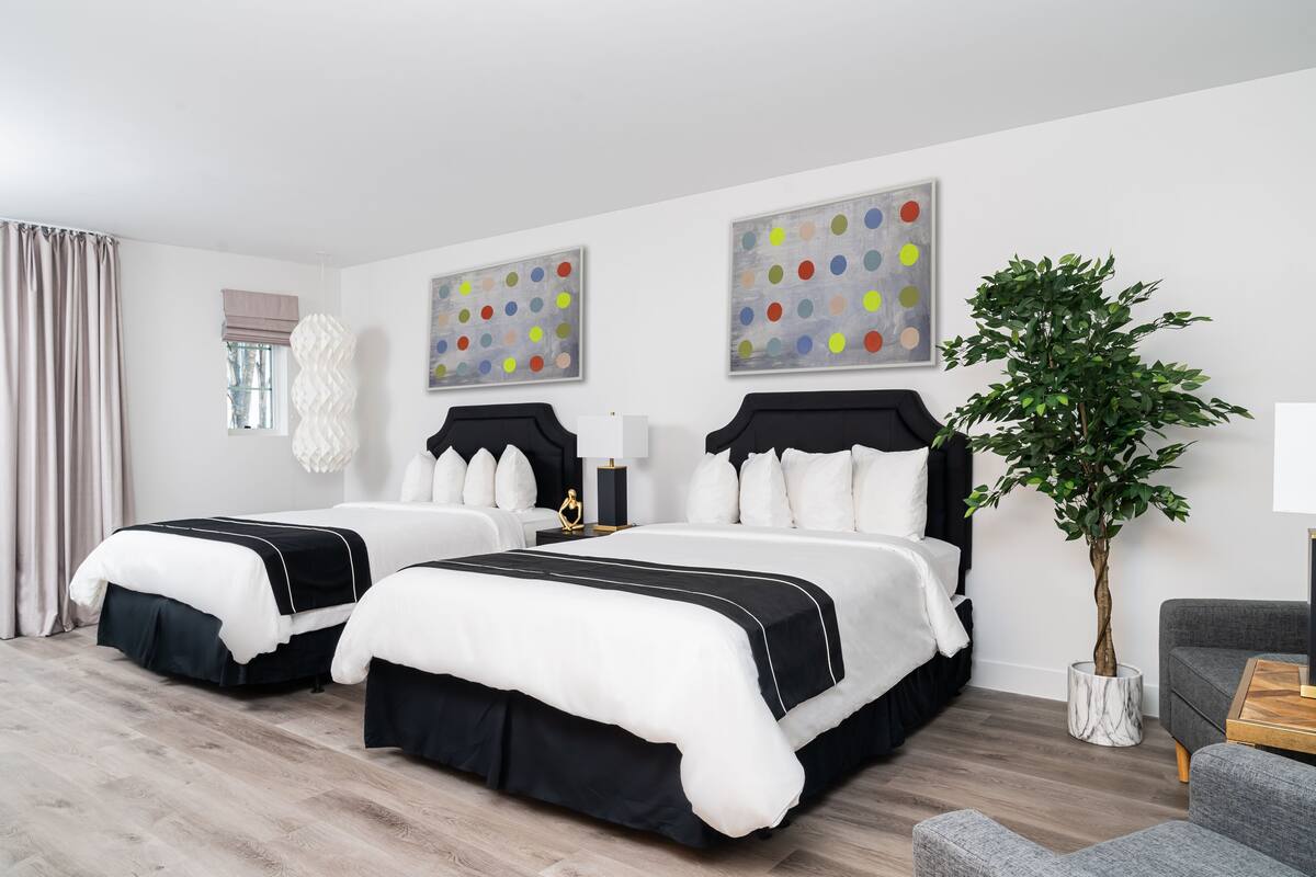 A hotel room with two beds, a potted plant, and artwork on the walls.