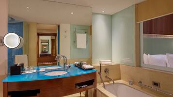 A modern bathroom with a blue countertop sink, a large mirror, and a bathtub.