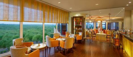 A modern dining area with a view of the forest, wooden flooring, and orange chairs.