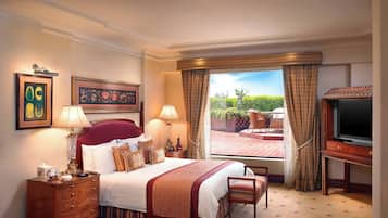 Relax in comfort with a large bed, bedside tables, and a TV, surrounded by a view of the outdoor area and lush greenery.