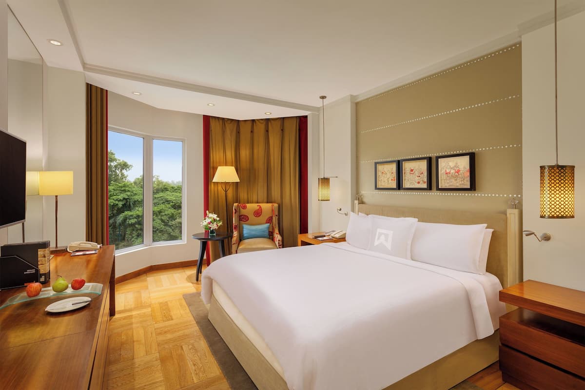 A hotel room with a large bed, a desk with a lamp, a chair, and a TV.