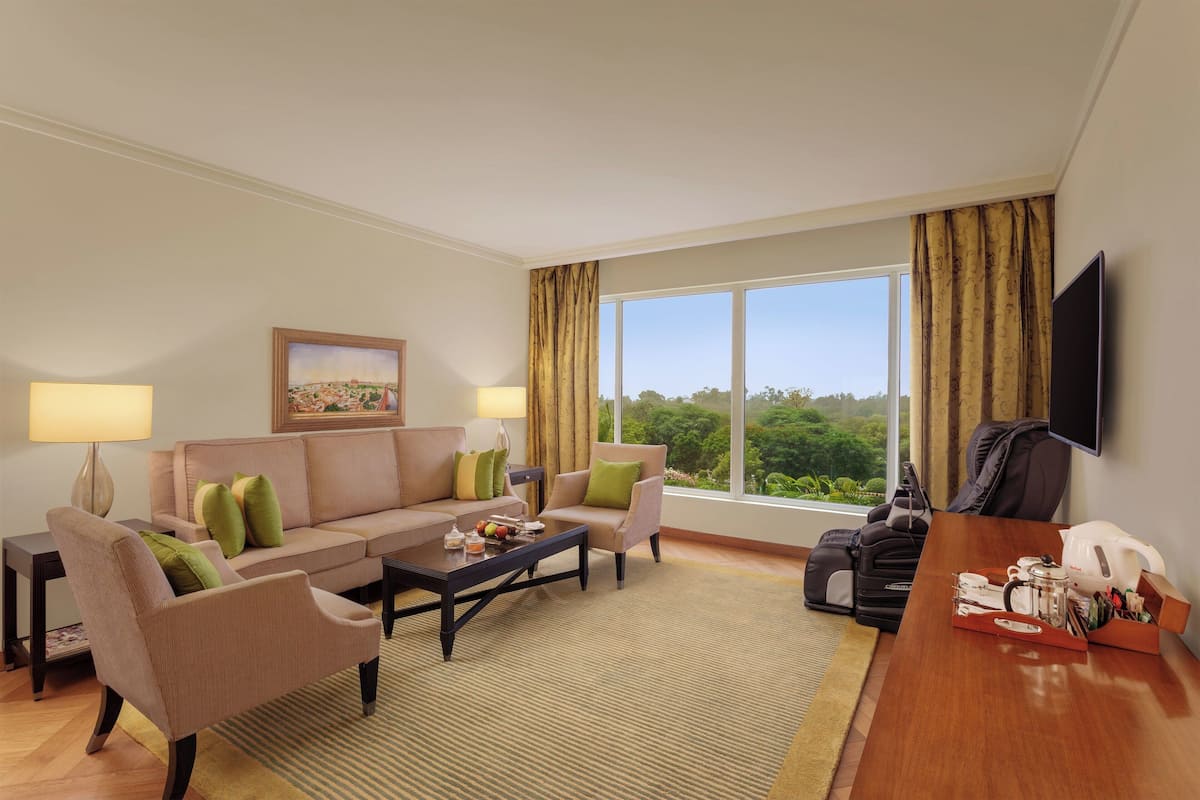 A hotel room with a sofa set, a coffee table, a TV, and a large window with curtains.