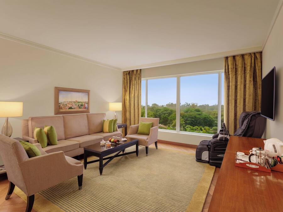 A hotel room with a sofa set, a coffee table, a TV, and a large window with curtains.