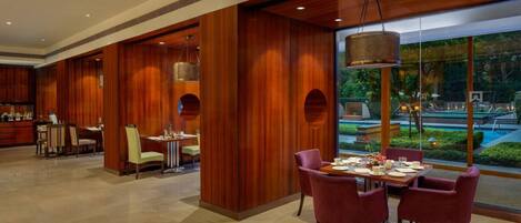 A modern dining area with wooden paneling, a large window with a view of a garden, and a table set for two.