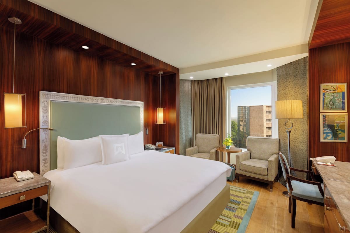A hotel room with a large bed, two armchairs, a desk, and a view of the city.