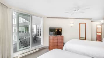 A hotel room with a large sliding glass door to a balcony, a ceiling fan, a flat-screen TV, a wooden dresser, and two beds.