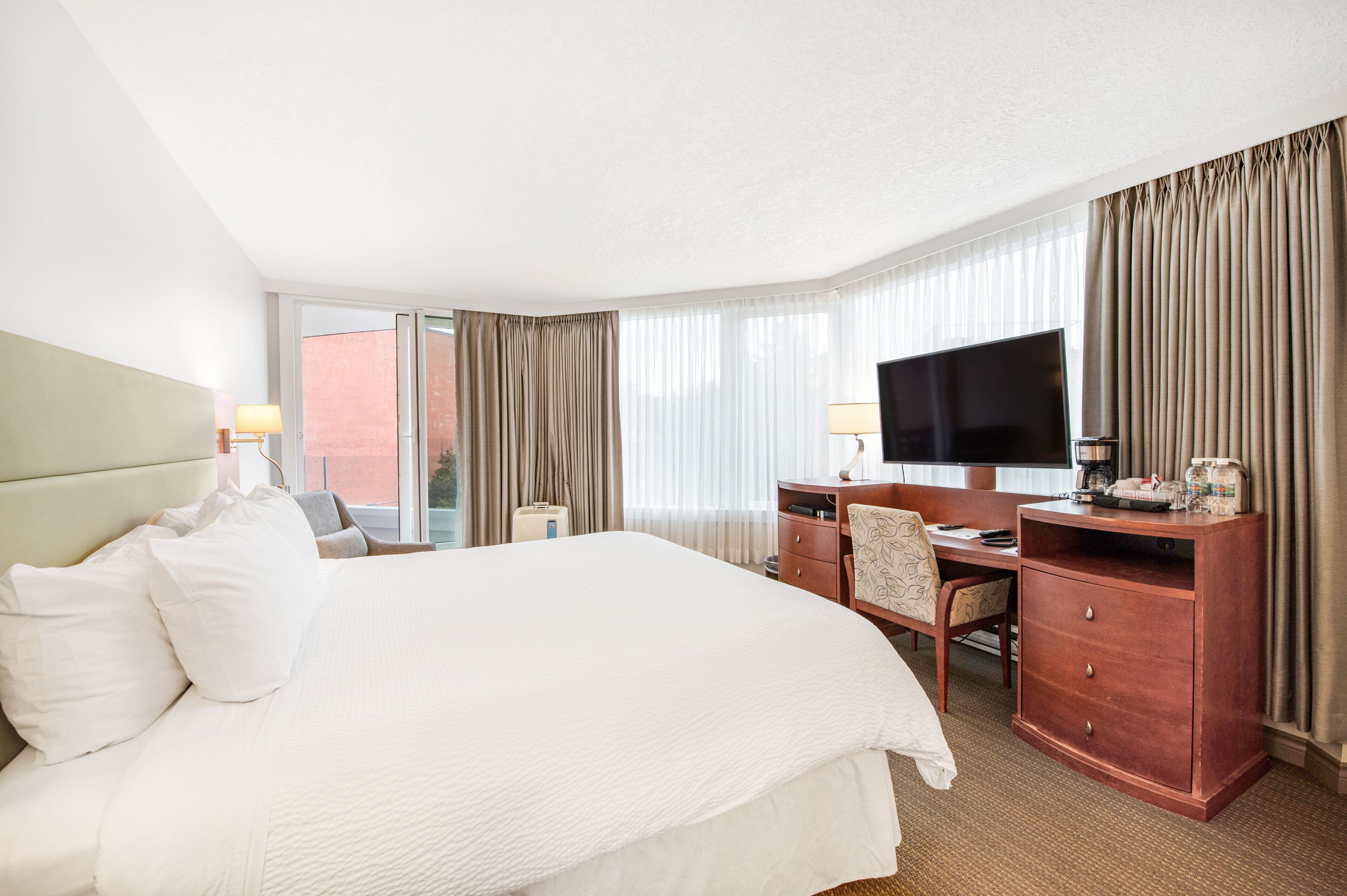 Habitación de hotel con una cama grande, un escritorio con televisor y vistas al exterior a través de amplias ventanas.