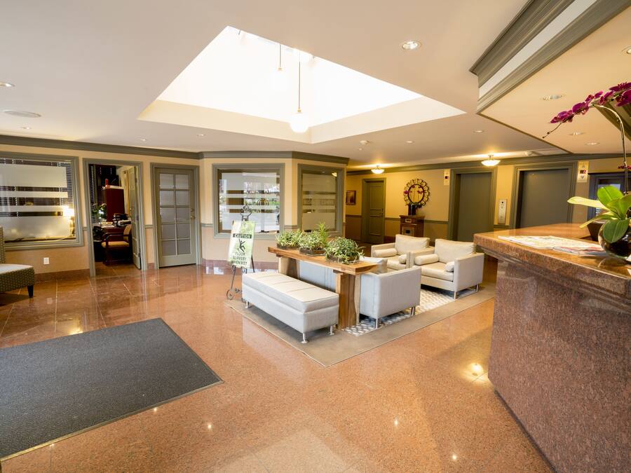 Een ruime lobby met een receptiebalie, zithoek en een glazen deur naar een business center.
