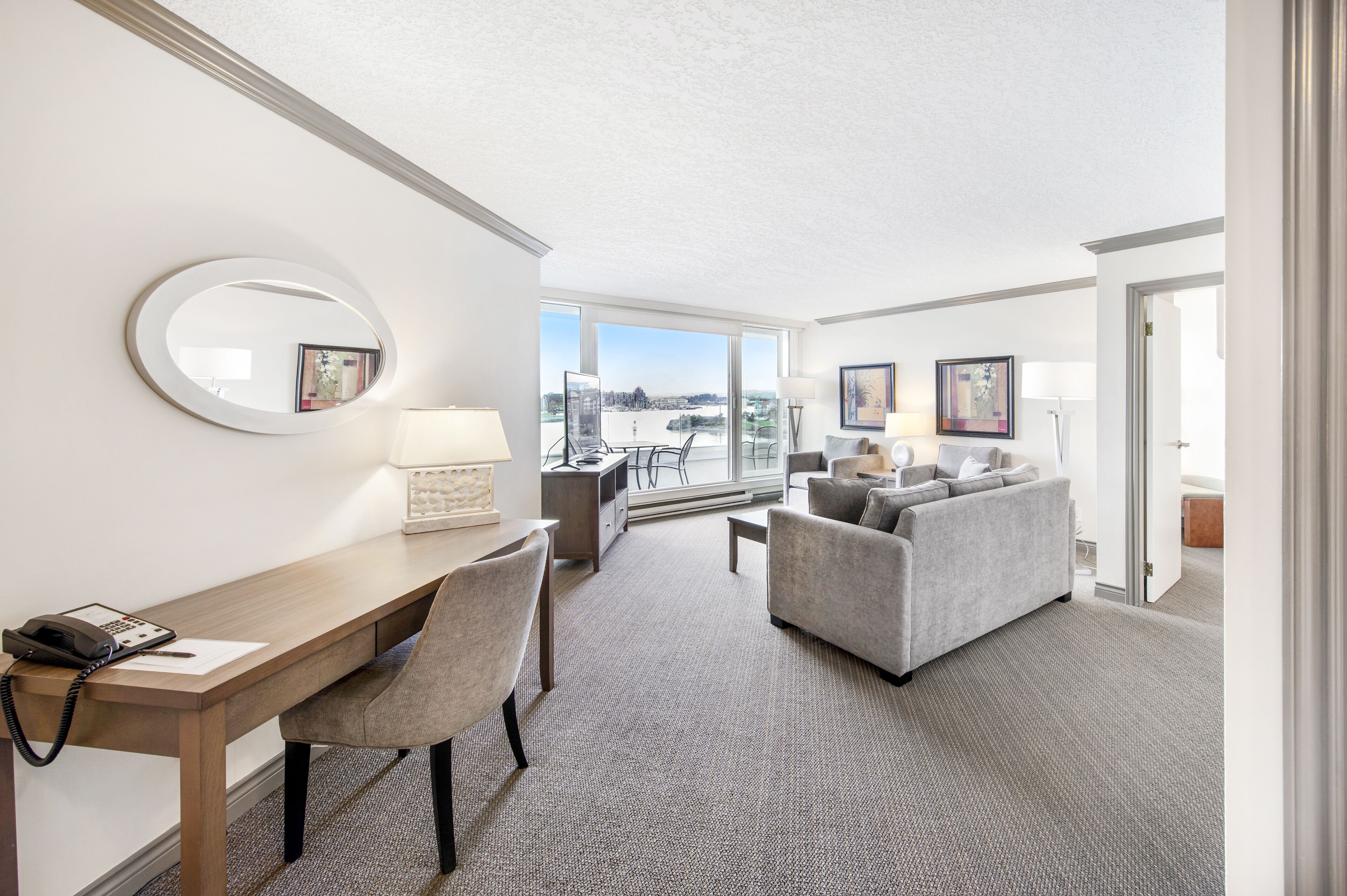 A hotel room with a desk, chair, sofa, and large windows offering a view of the outdoors.