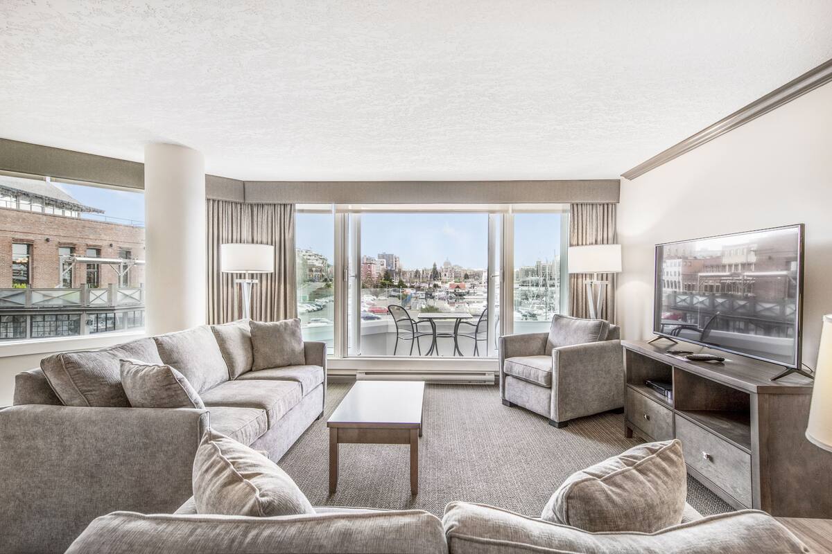 Ein modernes Hotelzimmer mit großem Fenster, einem Flachbildfernseher, einer Couch, einem Couchtisch und einem Schreibtisch.