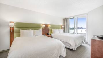 Hotelkamer met twee bedden, een groen hoofdeinde, een bureau en een groot raam met uitzicht op de stad.