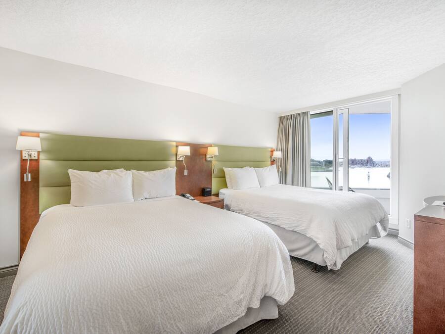 Hotelkamer met twee bedden, een groen hoofdeinde, een bureau en een groot raam met uitzicht op de stad.