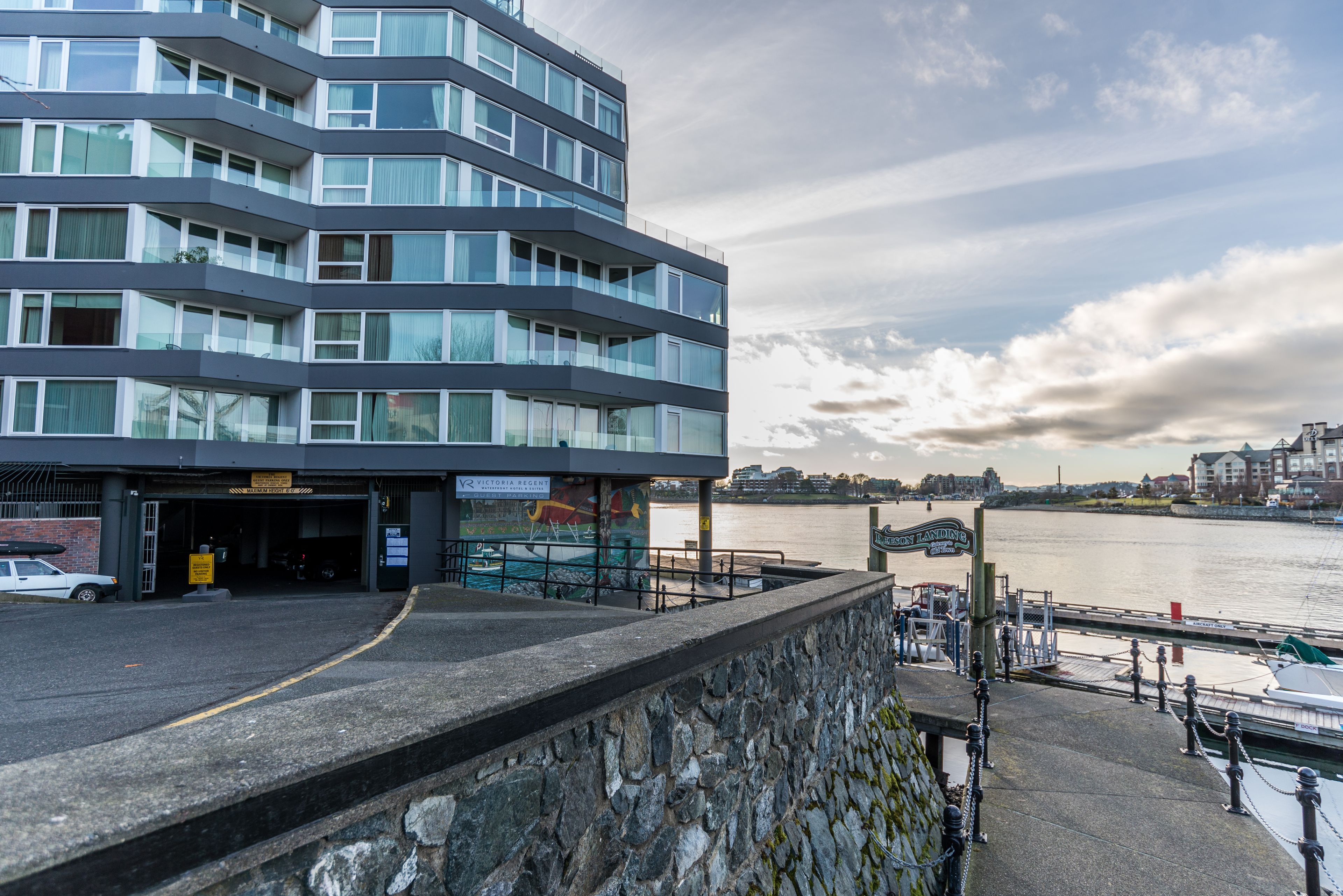 Um edifício moderno com vários andares e janelas amplas, situado perto de uma orla com um cais e barcos.