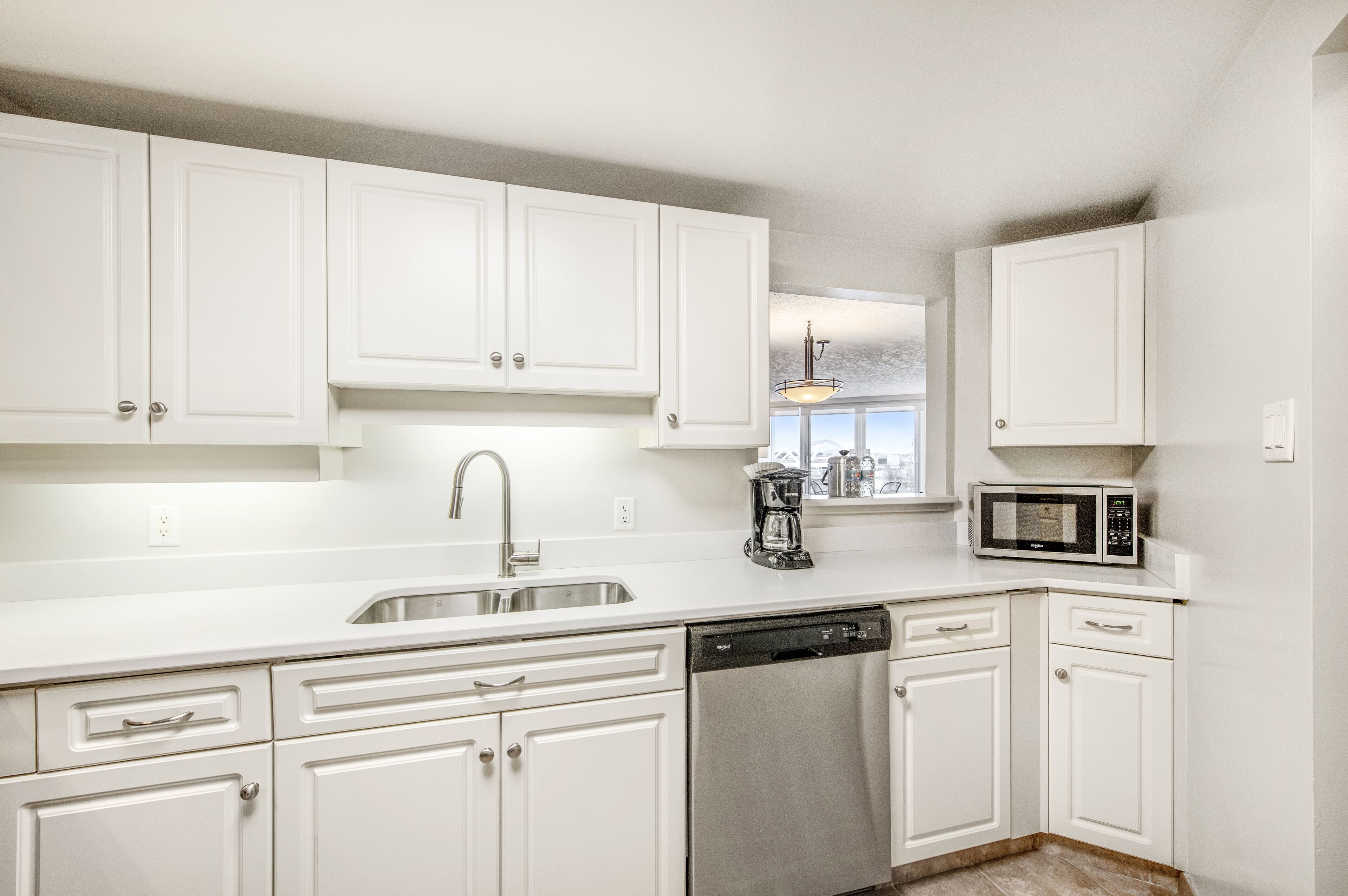 A modern kitchen with white cabinetry, a stainless steel sink, a coffee maker, and a microwave.