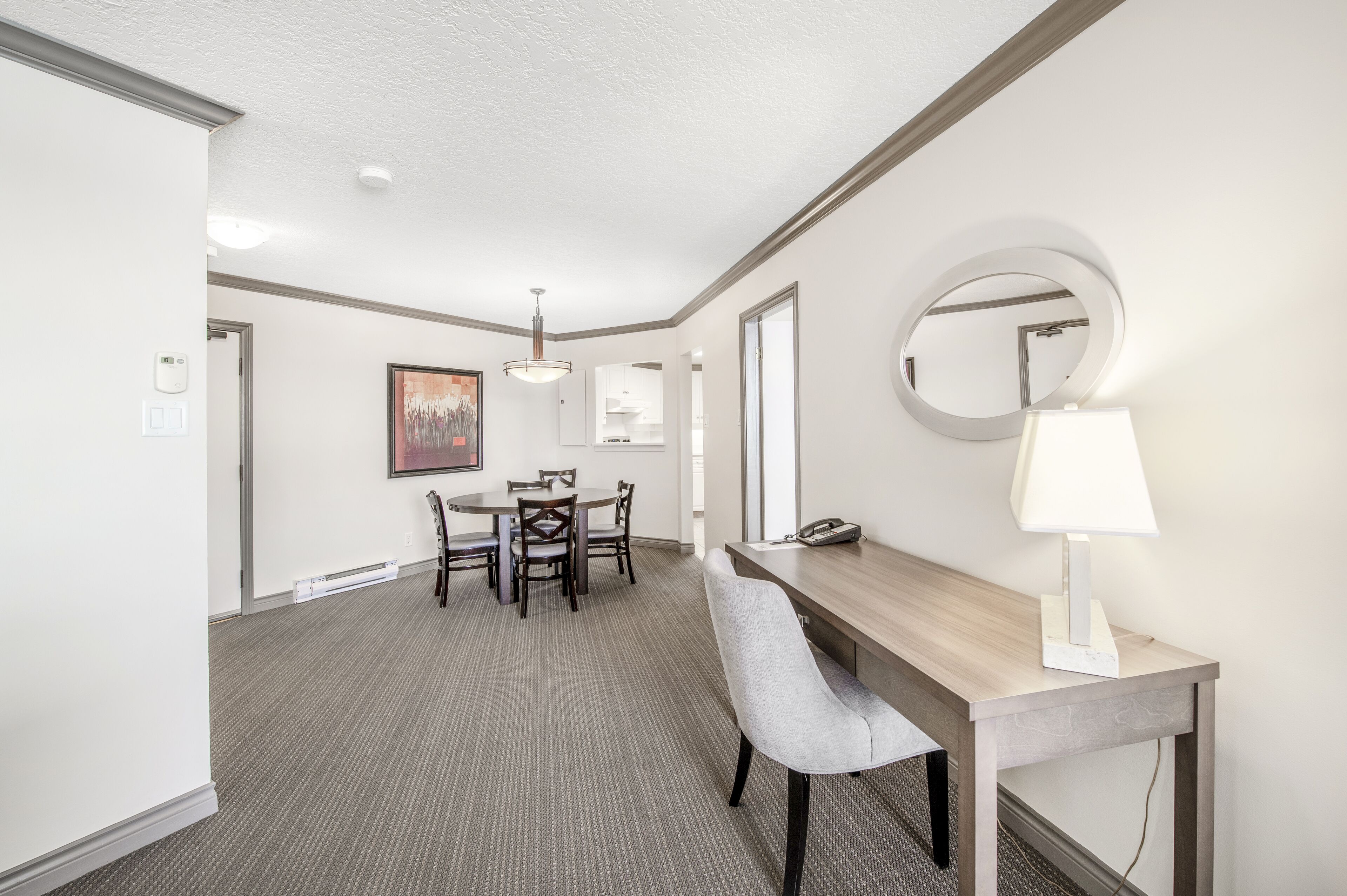 Une chambre d’hôtel avec un coin repas, un miroir rond, une lampe et un téléphone posés sur une table en bois.