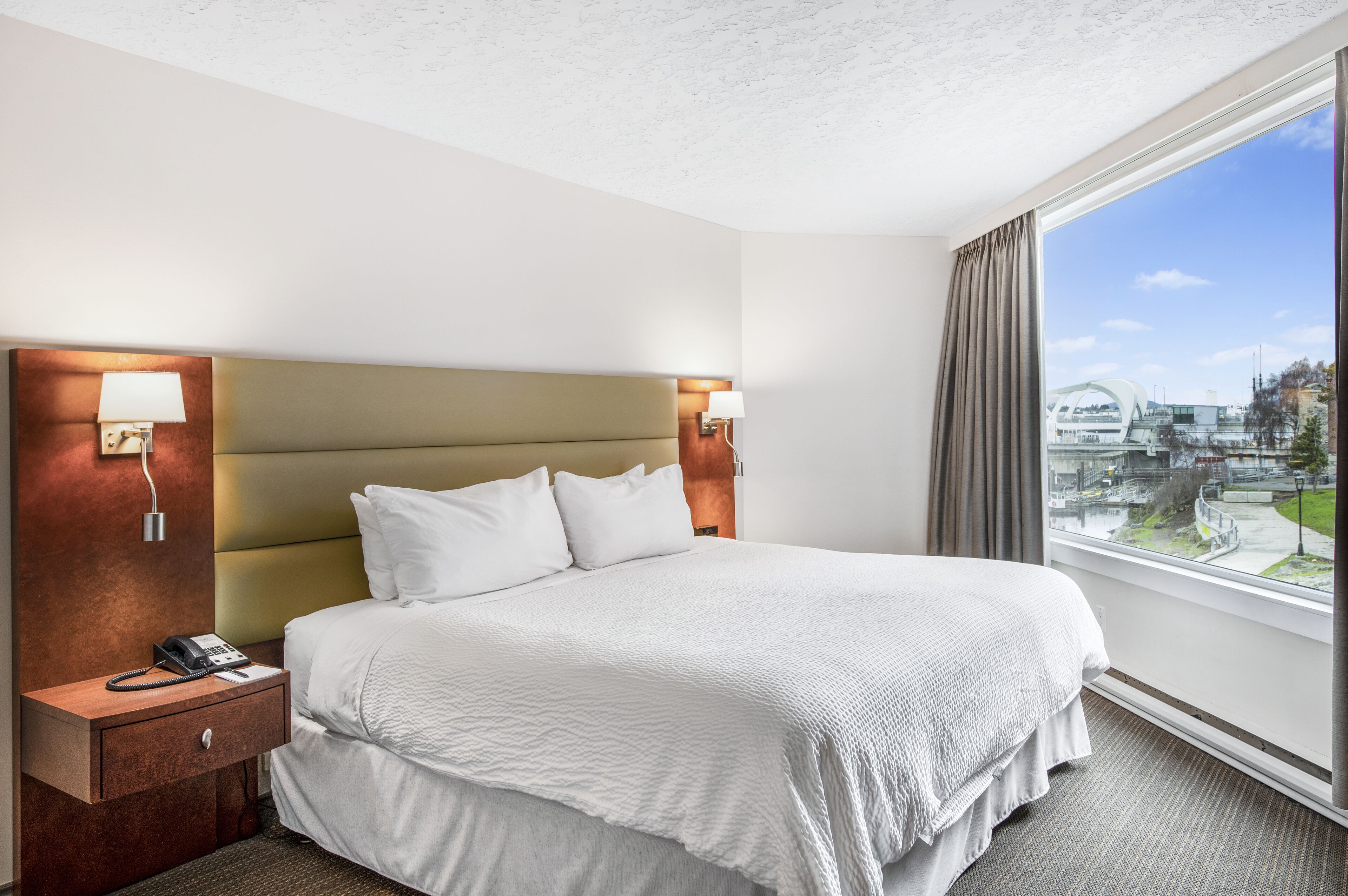 A hotel room with a large bed, two bedside lamps, a telephone, and a window with a city view.
