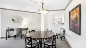 Habitación de hotel con una mesa redonda para comer, cuatro sillas, un escritorio con lámpara, un espejo y una obra de arte enmarcada en la pared.