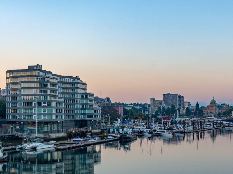 A waterfront marina with boats docked, a modern building with multiple floors, and a historic building with a dome in the background.