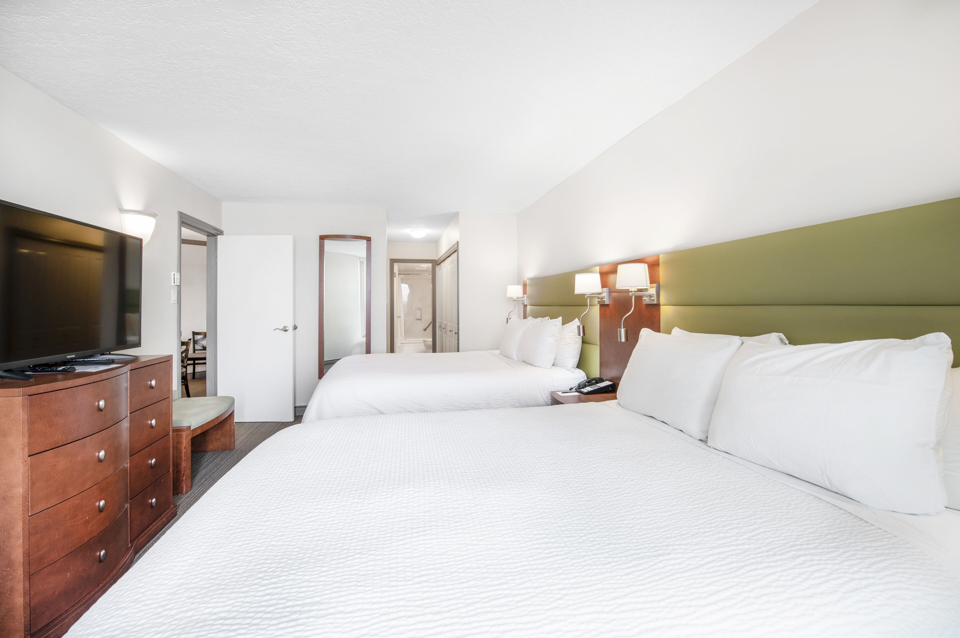 A hotel room with two beds, a TV, a dresser, and a desk with a lamp.