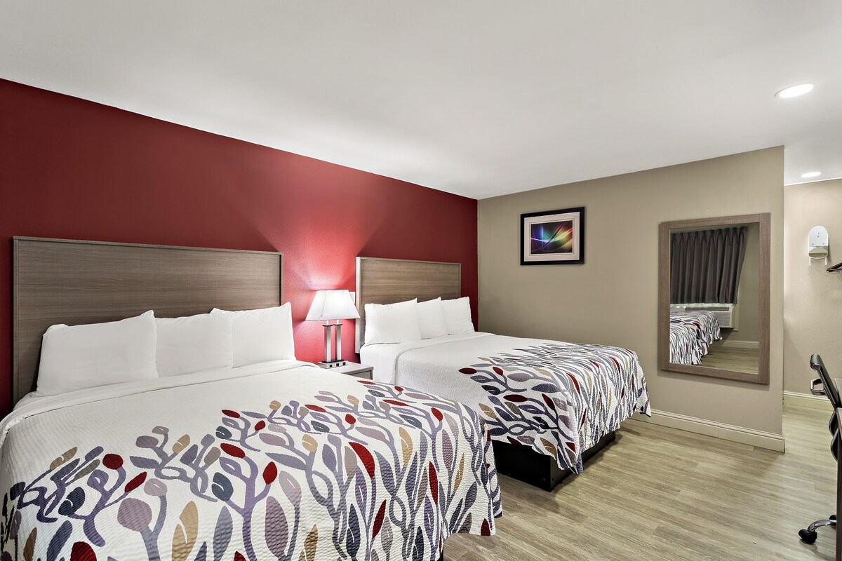 Habitación de hotel con dos camas, una mesita de noche, una lámpara, un espejo y un cuadro en la pared.