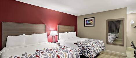 A hotel room with two beds, a nightstand, a lamp, a mirror, and a painting on the wall.