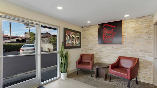 A hotel reception area with a glass door, two leather chairs, a small table, and a Red Roof Inn sign on the wall. - Red Roof Inn Redding (Redding)