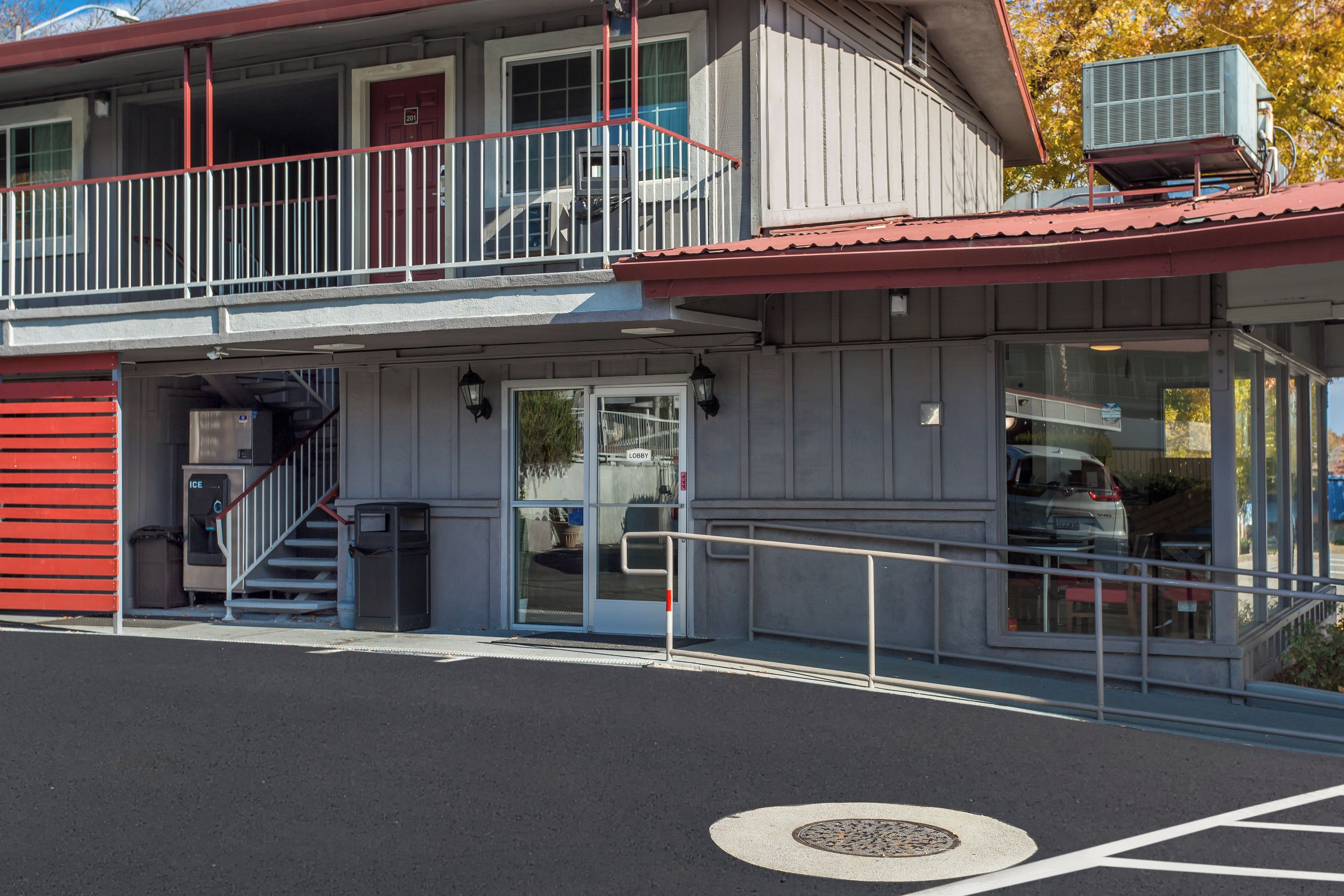 A two-story building with a red exterior, a balcony, and a ground-level entrance with a trash bin.