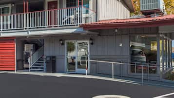 A two-story building with a red exterior, a balcony, and a ground-level entrance with a trash bin.