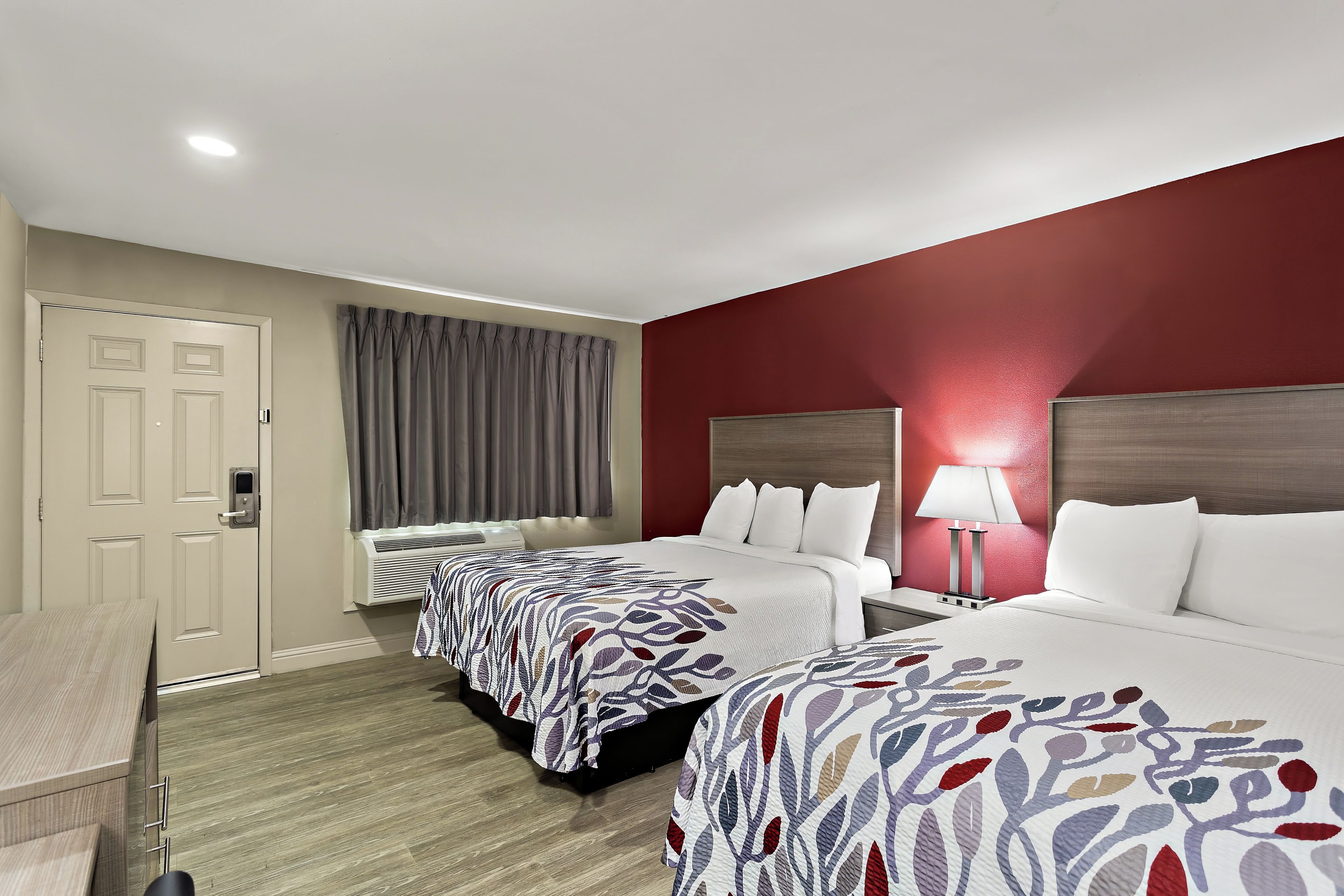 Una habitación de hotel con dos camas, un escritorio, una silla, una lámpara y una puerta.
