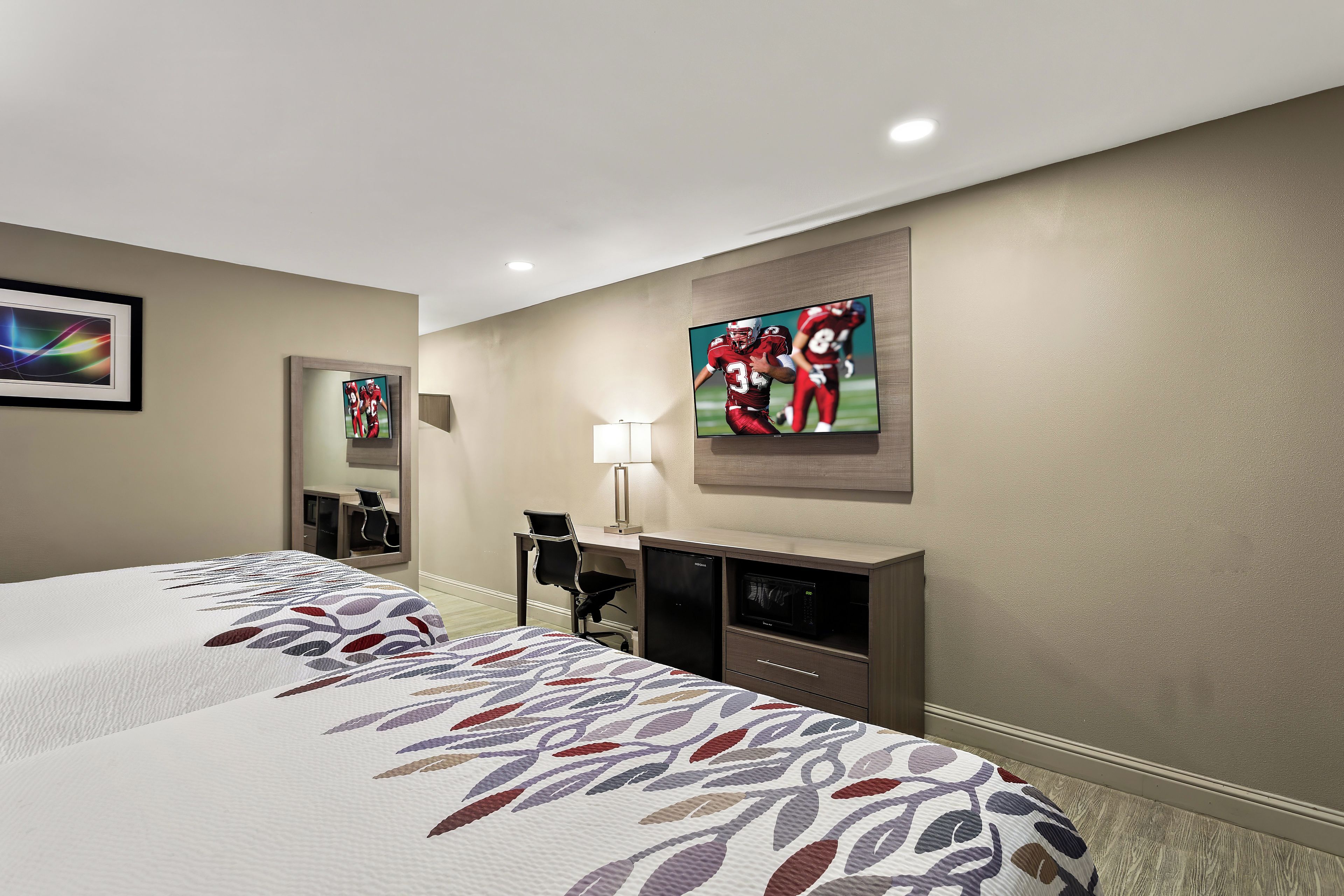 A hotel room with two beds, a desk, a chair, a television, and a microwave.