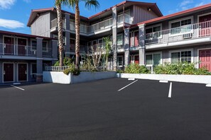 A multi-story hotel with balconies, a parking lot, and a landscaped area with plants. - Red Roof Inn Redding (Redding)