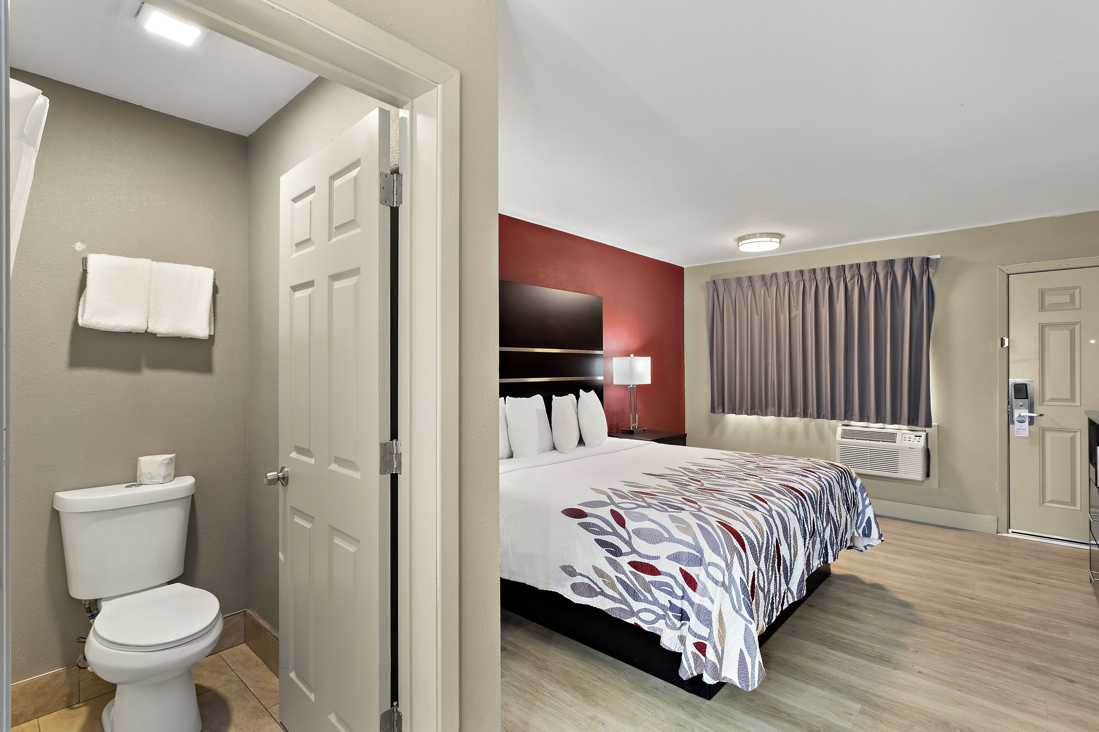 A hotel room with a bed, a bathroom with a toilet, and a door leading to another room.