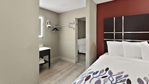 A hotel room with a bed, a bedside table, a mirror, and a clothing rack. - Red Roof Inn Redding (Redding)